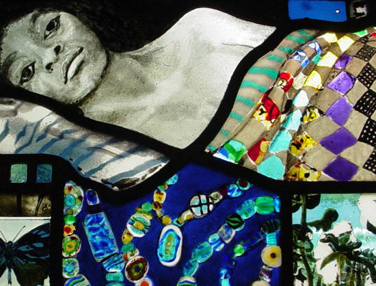 photgraphic detil of blues themed stained glss window shows woman under quilt and African trading beads